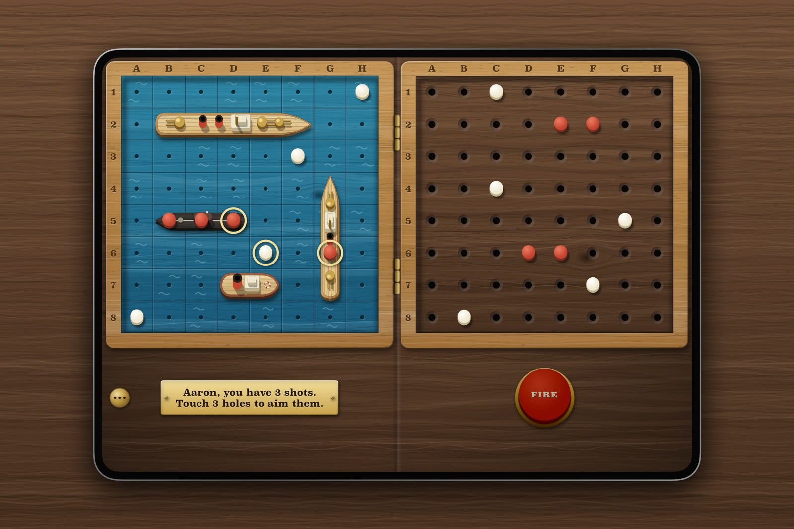 Knotty Navy on an open iPhone Duo lying on dark wood: a blue sea with four toy ships on one half, a dark peg board of shots on the other, and a red Fire plunger.